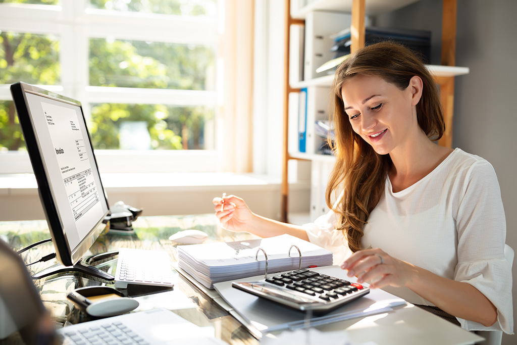 femme qui tape à la calculatrice et qui est devant un écran d