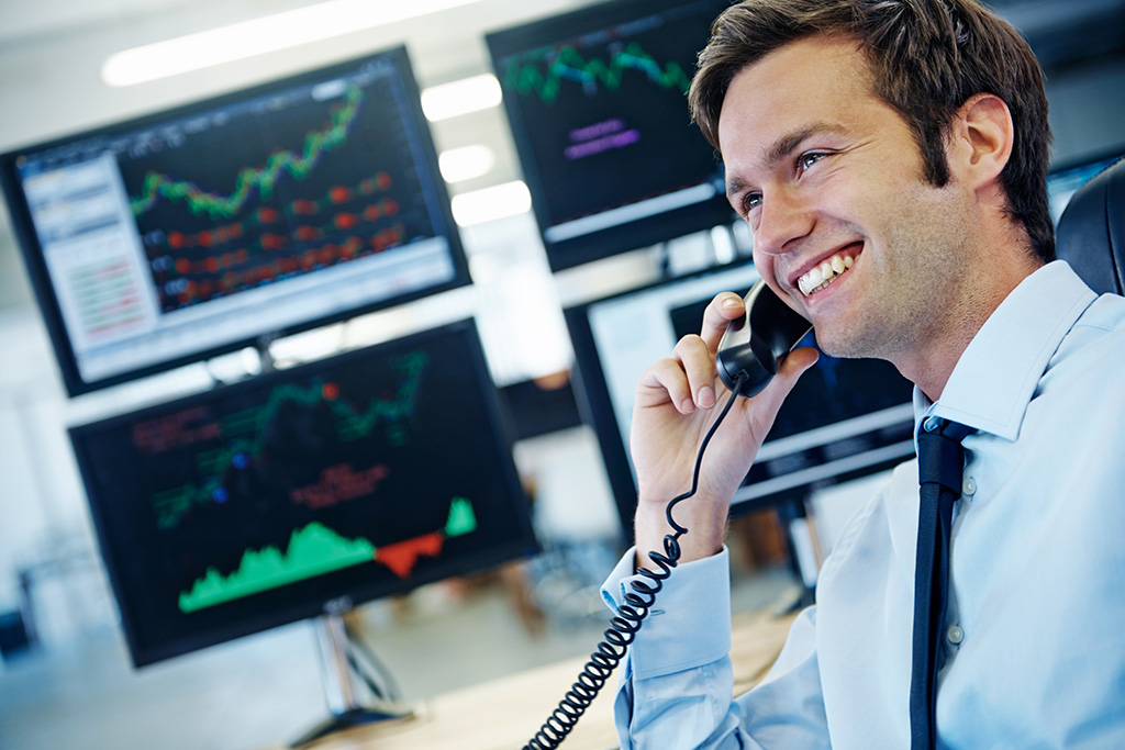 trader au téléphone devant 4 écrans d