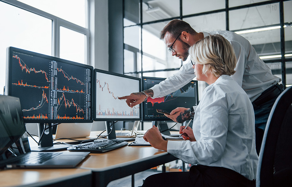 deux traders devant 3 écrans d