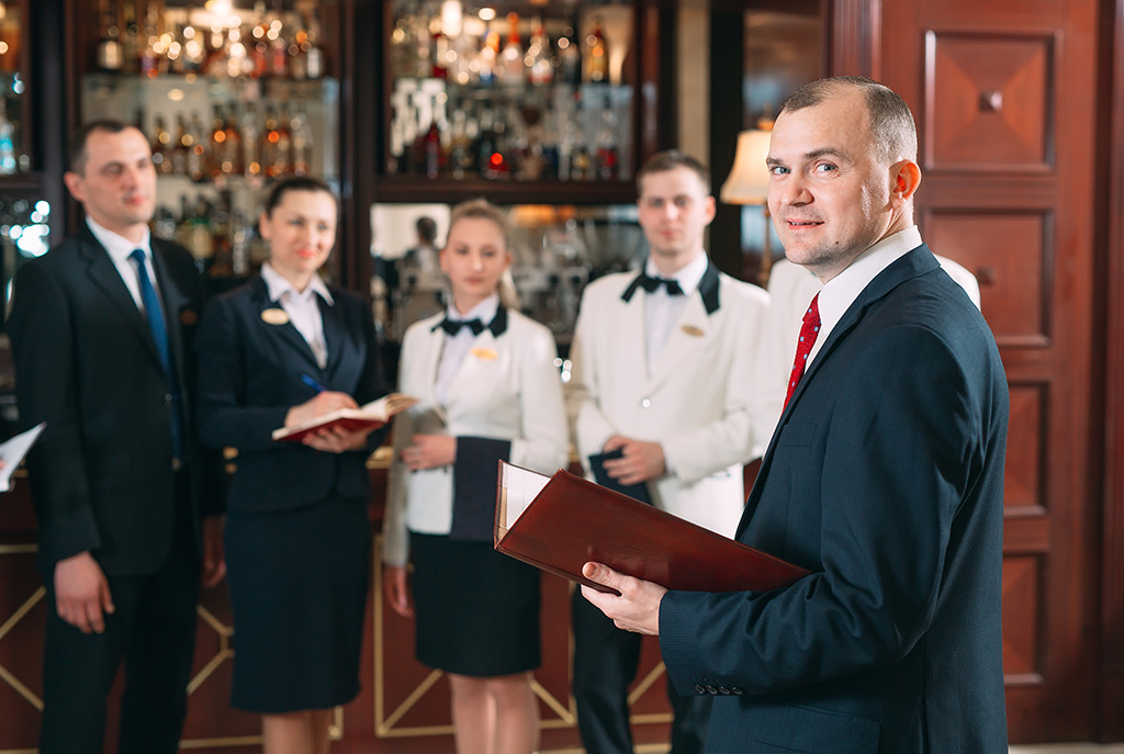 équipe de 5 personnes dont deux hommes serveurs et deux femme serveuses en arrière plan dans un restaurant et au premier plan le manager de cette équipe