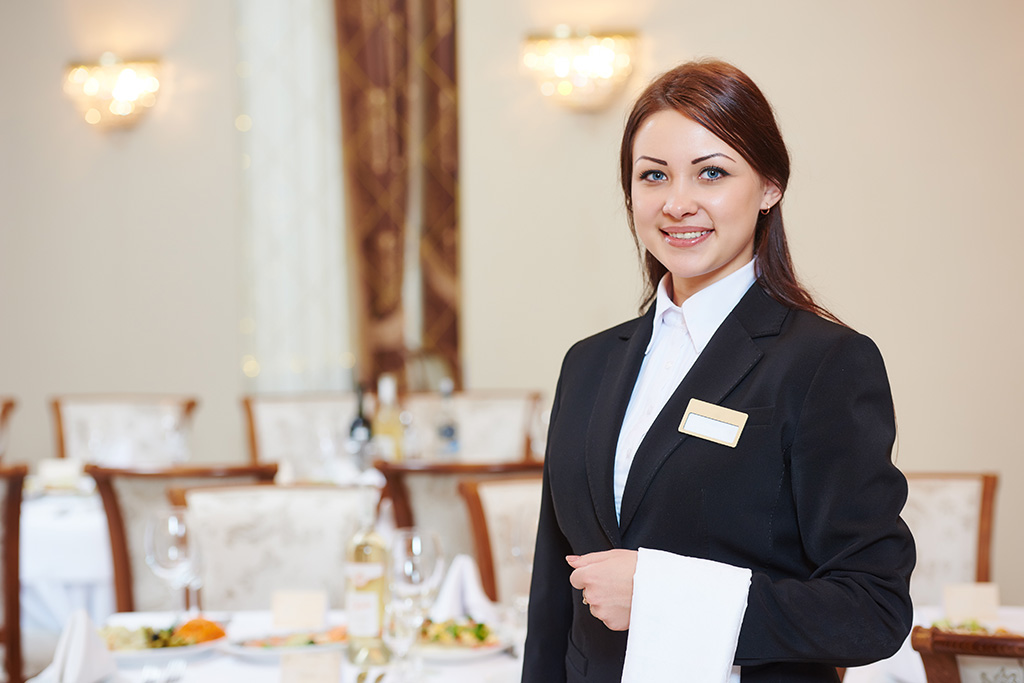 Femme serveuse habillée en tenue qui sourit dans une salle de restaurant