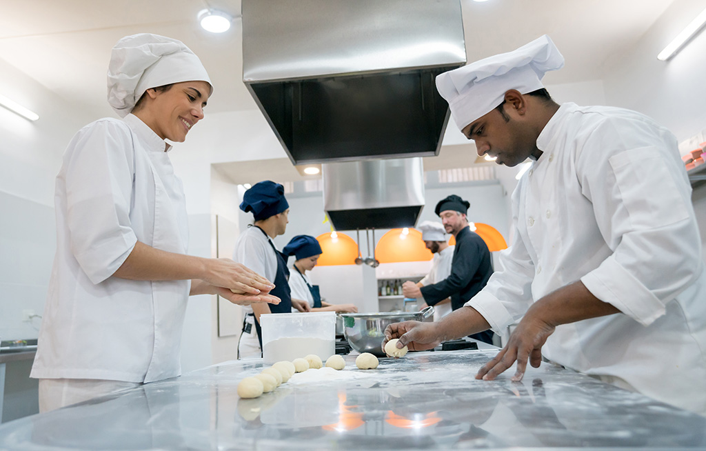 équipe de 6 personnes hommes et femmes dans une cuisine de restauration collective qui cuisinent