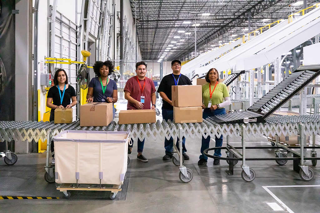 équipe logistique de 5 personnes dont 3 femmes et deux hommes se tenant devant un tapis roulant de chargement de colis