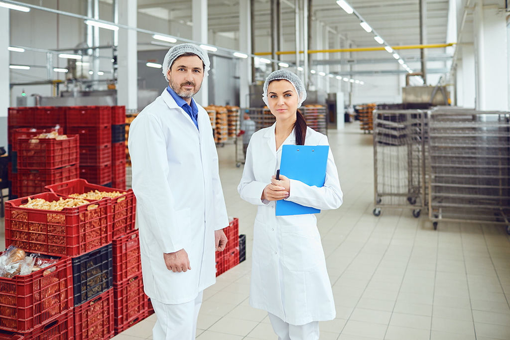 équipe contrôle qualité d'un homme et d'une femme en blouse blanche avec une charlotte sur la tête dans un entrepôt