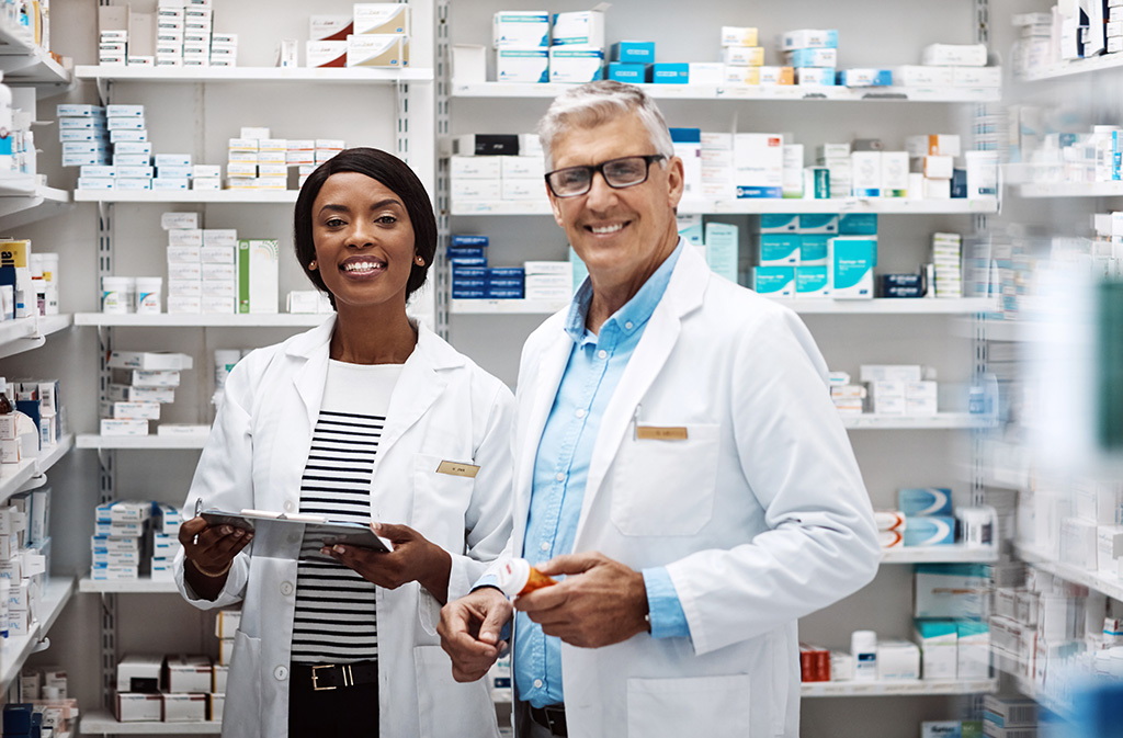 un homme et une femme en blouse blanche qui sourient dans la salle de préparation en pharmacie