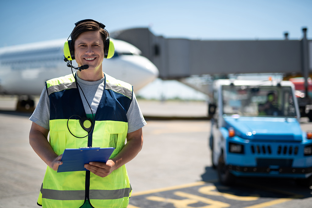 agent de transit aérien souriant portant un casque avec micro et un gilet jaune portant un bloc note dans les mains et dans l