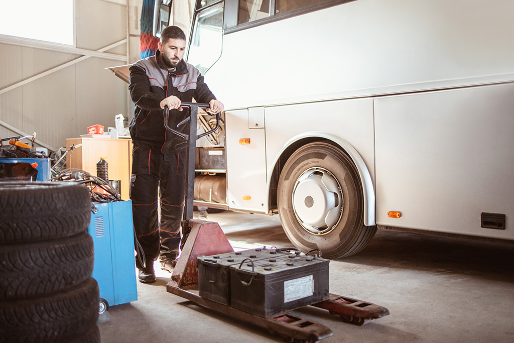 dans un grand garage technicien de maintenance de bus qui transporte sur un transpalette une batterie de bus