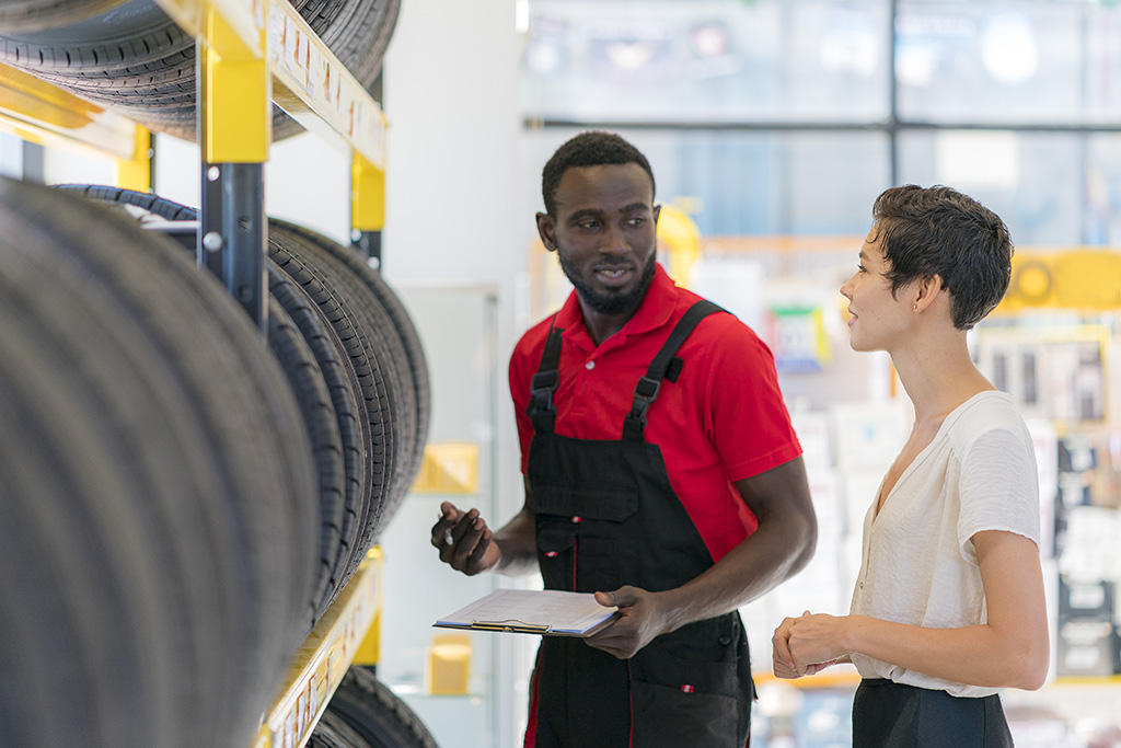 Vendeur service après-vente auto discutant devant un présentoir de pneus avec une cliente