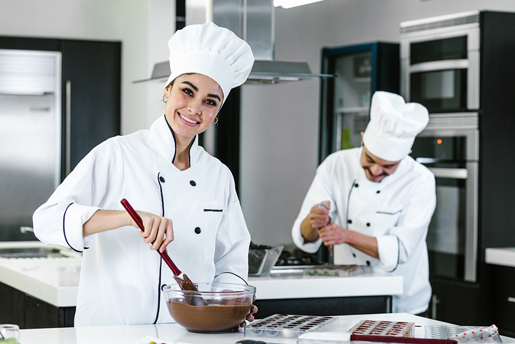 dans leur atelier deux chocolatiers homme et femme entrain de travailler à la spatule du chocolat dans un saladier