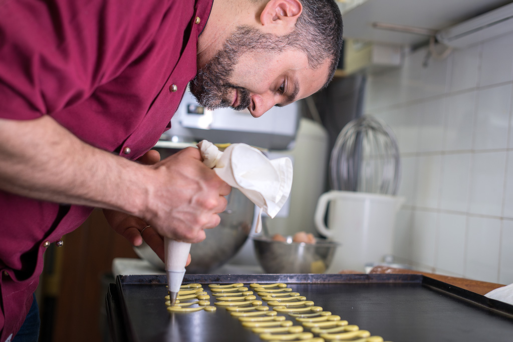 pâtissier dans son atelier entrain de pocher à la poche à douille des pâtisseries