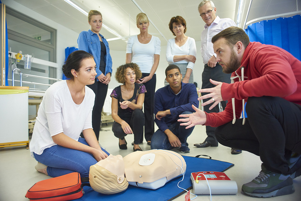 groupe de personnes homme et femme de tout âge autour d'un mannequin pour une formation de massage cardiaque